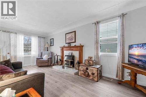 Wood-finish flooring, fireplace with a decorative wooden mantel, tiled hearth, and dual windows with window blinds - 143 Walter Avenue S, Hamilton, ON 