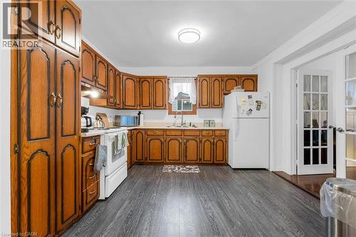 Kitchen featuring wood cabinetry, solid surface countertops, dual-basin sink with a gooseneck faucet, wood-finish flooring, and French doors - 143 Walter Avenue S, Hamilton, ON 