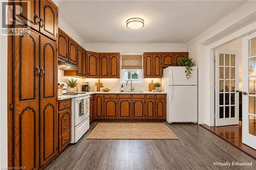 Kitchen featuring stained wood cabinetry, wood-finish flooring, white appliances, under-cabinet lighting, and French doors - 143 Walter Avenue S, Hamilton, ON 
