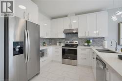 Kitchen featuring white high-gloss cabinetry, stainless steel appliances, quartz countertops, a patterned tile backsplash, and light-toned floor tiling - 