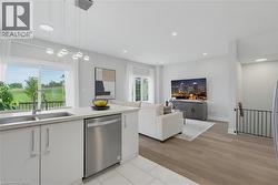 Open-concept interior featuring wood-finish flooring, white cabinetry, stainless steel dishwasher, modern multi-pendant lighting, and recessed ceiling lights - 