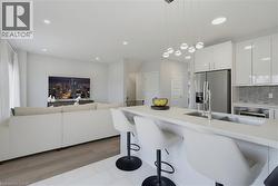 Kitchen featuring white gloss cabinetry, quartz countertops, a modern pendant light fixture, stainless steel refrigerator, and tiled backsplash - 