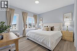Bedroom featuring wood-finish flooring, neutral wall paint, and multiple windows with curtain rod hardware and attached lighting - 