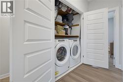 Laundry closet featuring dual white sliding doors, wood-finish flooring, built-in shelving, and front-loading appliances - 