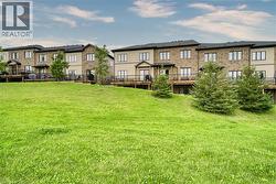 Multi-unit building exterior featuring a brick and vertical siding facade, elevated wooden decks with metal railings, and expansive common green space with mature evergreen trees - 