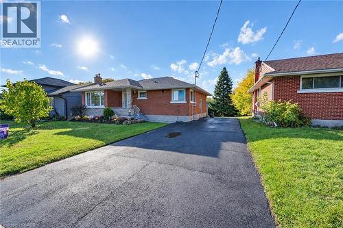 Single-story residence featuring a red brick exterior, shingled roof, asphalt driveway, and manicured front lawn - 46 Traynor Avenue, Kitchener, ON 