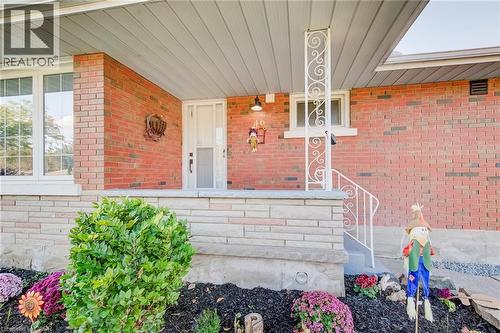 Covered front porch featuring a red brick facade, decorative wrought iron support column, stone masonry base, and a glass-paneled entry door - 46 Traynor Avenue, Kitchener, ON 