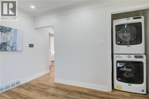 Laundry area featuring stacked white front-loading appliances and wood-finish flooring - 46 Traynor Avenue, Kitchener, ON 