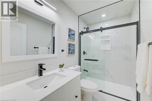 Bathroom featuring a vanity with a solid-surface countertop, rectangular integrated sink, matte black faucet, walk-in shower with floor-to-ceiling surround and sliding glass door, and integrated showe - 46 Traynor Avenue, Kitchener, ON 