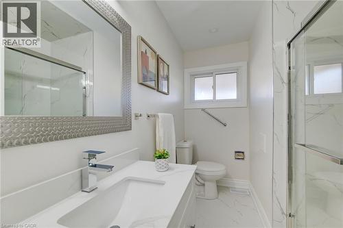 Bathroom featuring a vanity with a white solid-surface countertop, rectangular basin, polished chrome faucet, large framed mirror, and floor-to-ceiling stone-patterned tile shower surround - 46 Traynor Avenue, Kitchener, ON 