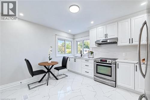 Kitchen featuring white shaker-style cabinetry, stainless steel range with overhead hood, stone-finish countertops, and large-format porcelain tile flooring - 46 Traynor Avenue, Kitchener, ON 