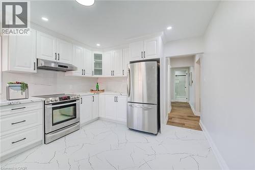 Kitchen featuring white shaker-style cabinetry, stainless steel appliances, stone-finish countertops, stone-patterned floor tile, and a glass-paneled cabinet door - 46 Traynor Avenue, Kitchener, ON 