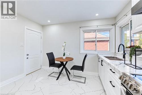Kitchen area featuring white shaker-style cabinetry, patterned stone-finish countertops, a dual-basin stainless steel sink with a matte black faucet, recessed lighting, and tile flooring - 46 Traynor Avenue, Kitchener, ON 