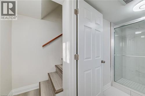 Walk-in shower featuring a glass enclosure and wall-surround tiles, stairs with wood-finish flooring, and a wooden handrail - 46 Traynor Avenue, Kitchener, ON 