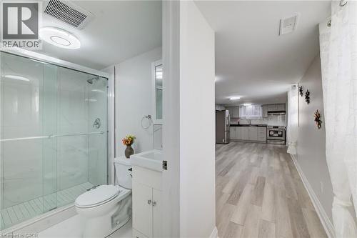 Bathroom featuring a glass-enclosed shower with tile surround and a white vanity with integrated basin, combined with wood-finish flooring and kitchen cabinetry with stainless steel appliances - 46 Traynor Avenue, Kitchener, ON 