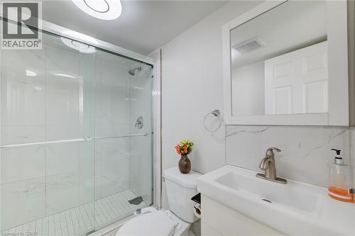 Bathroom featuring a walk-in glass-enclosed shower with full-height stone-finish tile surround, white vanity with integrated sink, polished metal faucet, and framed mirror - 46 Traynor Avenue, Kitchener, ON 