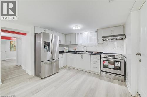Kitchen featuring white cabinetry, dark countertops, a stone-pattern backsplash, stainless steel appliances, and wood-finish flooring - 46 Traynor Avenue, Kitchener, ON 