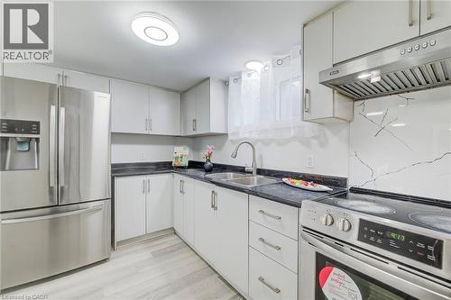 Kitchen featuring white cabinetry, dark stone-finish countertops, stainless steel appliances, a patterned stone-look backsplash, and wood-finish flooring - 46 Traynor Avenue, Kitchener, ON 