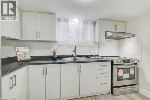 Kitchen featuring flat-panel cabinetry, dark stone countertops, stainless steel range with overhead ventilation, and a double-basin stainless steel sink - 46 Traynor Avenue, Kitchener, ON 