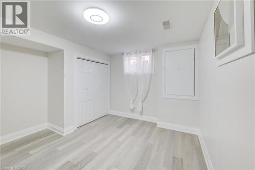 Neutral-toned interior featuring wood-finish flooring, double-door closet cabinetry, a ceiling-mounted LED light fixture, and an egress-style window - 46 Traynor Avenue, Kitchener, ON 