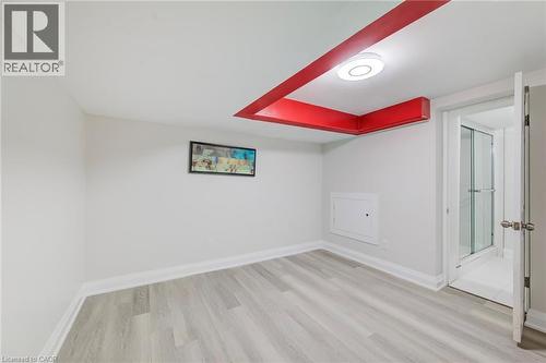 Interior space featuring wood-finish flooring, a recessed ceiling accent with integrated flush-mount lighting, and a doorway opening to a glass-enclosed shower - 46 Traynor Avenue, Kitchener, ON 