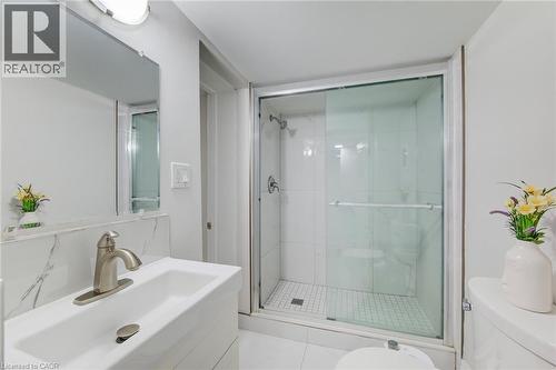 Bathroom featuring a white vanity with a rectangular sink, brushed nickel faucet, large wall-mounted mirror, and a walk-in shower with glass sliding doors and tile surround - 46 Traynor Avenue, Kitchener, ON 