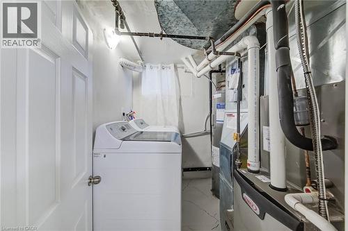 Utility area featuring a natural gas furnace, water heater, and washer and dryer hookups with painted concrete flooring - 46 Traynor Avenue, Kitchener, ON 
