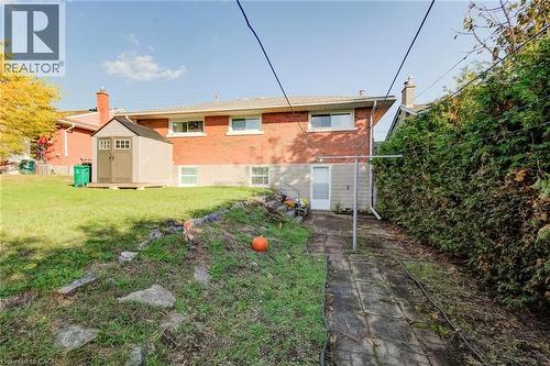 Rear exterior featuring red brick masonry, stone retaining wall, paved walkway, and a storage shed - 46 Traynor Avenue, Kitchener, ON 