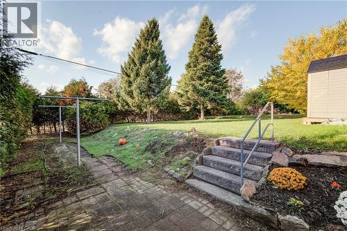 Expansive backyard featuring a tiered lawn, stone retaining wall, paved patio, mature evergreen trees, and granite slab steps with metal handrails - 46 Traynor Avenue, Kitchener, ON 