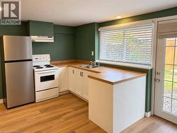 Compact kitchen featuring wood-finish flooring, white cabinetry, a stainless steel refrigerator, and a white electric range with an overhead vent - 