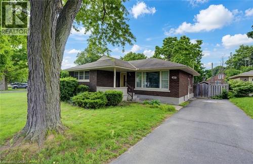 Single-story brick exterior featuring a covered front entryway, expansive lawn, mature tree, and asphalt driveway - 244 Royal Street, Waterloo, ON 