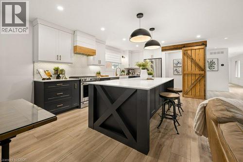 Kitchen featuring a central island with X-brace detailing, white and dark cabinetry, wood-finish flooring, a custom range hood, and a sliding barn door - 361 Lee Circle, Waterloo, ON 
