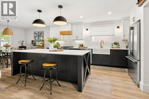Kitchen featuring a central island with a solid-surface countertop, apron-front farmhouse sink, herringbone-pattern tile backsplash, wood-finish flooring, and two-tone cabinetry - 361 Lee Circle, Waterloo, ON 