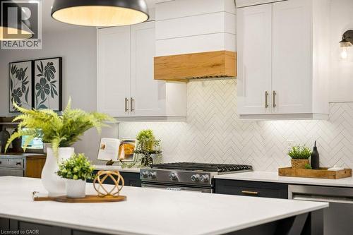 Kitchen featuring white Shaker-style cabinetry, a custom range hood with wood accents, a herringbone-patterned tile backsplash, a center island with a stone-finish countertop, and brushed metal hardwa - 361 Lee Circle, Waterloo, ON 