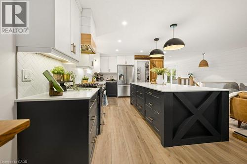Kitchen featuring white and black shaker-style cabinetry, white stone-finish countertops, a large island with X-frame detailing, herringbone-patterned tile backsplash, and wood-finish flooring - 361 Lee Circle, Waterloo, ON 