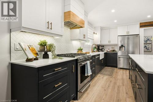 Kitchen featuring two-tone cabinetry with gold-tone hardware, quartz countertops, herringbone-patterned tile backsplash, wood-finish flooring, and a range hood with natural wood accents - 361 Lee Circle, Waterloo, ON 