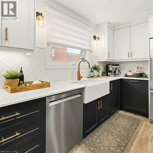 Kitchen featuring two-tone cabinetry with brass-finish hardware, quartz countertops, herringbone tile backsplash, and a white farmhouse sink with a brass-finish faucet - 361 Lee Circle, Waterloo, ON 