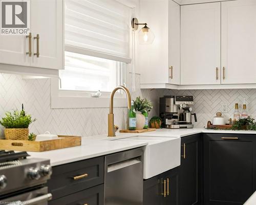 Kitchen featuring contrasting cabinetry, quartz countertops, white farmhouse sink, herringbone-patterned tile backsplash, and brass-finish hardware - 361 Lee Circle, Waterloo, ON 