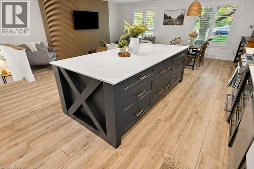 Kitchen island featuring a white countertop, charcoal-toned cabinetry with X-brace detailing, and metallic hardware, complemented by wood-finish flooring, white shiplap walls, and a vertical wood-slat - 361 Lee Circle, Waterloo, ON 