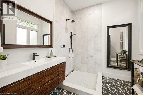 Bathroom featuring a dark wood-finish vanity with an integrated basin, walk-in shower with large-format wall tile, matte black rainfall showerhead, and geometric patterned floor tile - 361 Lee Circle, Waterloo, ON 