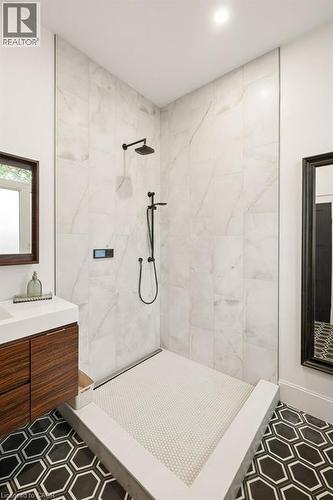 Walk-in shower featuring floor-to-ceiling large-format tile, matte black rainfall shower head with handheld attachment, custom stone-finish base with penny-round tiling, and floating wood-finish vanit - 361 Lee Circle, Waterloo, ON 