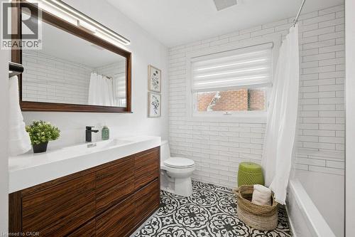 Bathroom featuring a wood-finish vanity with a rectangular sink, matte black faucet, patterned tile flooring, and white subway-style wall tile - 361 Lee Circle, Waterloo, ON 