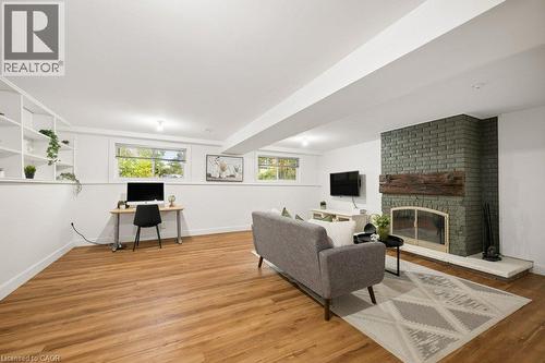 Painted brick fireplace with a rustic timber mantel and stone hearth, wood-finish flooring, built-in shelving, and recessed ceiling lighting - 361 Lee Circle, Waterloo, ON 