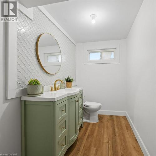 Sage green vanity with integrated sink and brass hardware, wall-mounted circular mirror, scallop-pattern tile backsplash, and wood-finish flooring - 361 Lee Circle, Waterloo, ON 