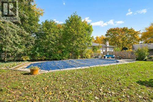 Rear grounds featuring a rectangular in-ground swimming pool, stone-paver hardscaping, mature trees, and wooden perimeter fencing - 361 Lee Circle, Waterloo, ON 