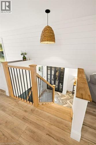 Staircase featuring wood-finish flooring, white shiplap walls, a natural fiber woven pendant light, and a railing with wooden handrails and black metal balusters - 361 Lee Circle, Waterloo, ON 