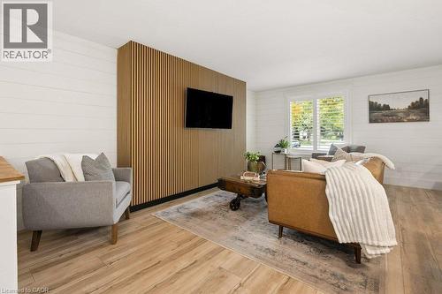 Bright, open living space featuring warm wood-finish flooring, a custom wood-slat accent wall with integrated flat-screen television, and large windows with natural light - 361 Lee Circle, Waterloo, ON 