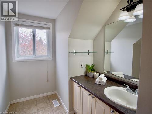 Bathroom vanity featuring a dark solid-surface countertop, an integrated oval basin, light-toned cabinetry, a wall-mounted glass shelf, and a multi-bulb light fixture - 449 Exmoor Street, Waterloo, ON 
