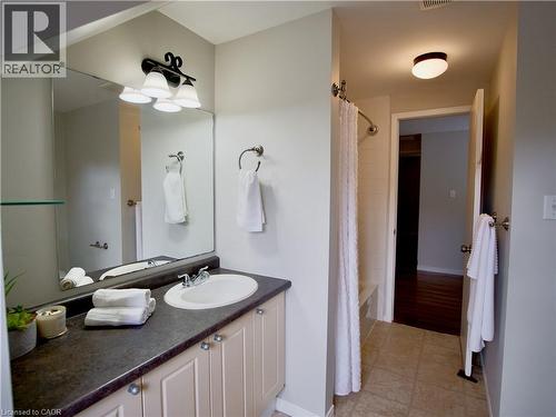 Bathroom featuring a vanity with dark countertop, undermount sink, three-light decorative fixture, large wall-mounted mirror, and tile flooring - 449 Exmoor Street, Waterloo, ON 