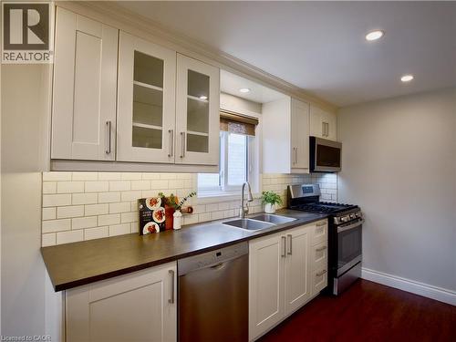 Kitchen featuring white shaker-style cabinetry with glass-panel inserts, subway tile backsplash, dark solid-surface countertops, stainless steel appliances, and wood-finish flooring - 449 Exmoor Street, Waterloo, ON 